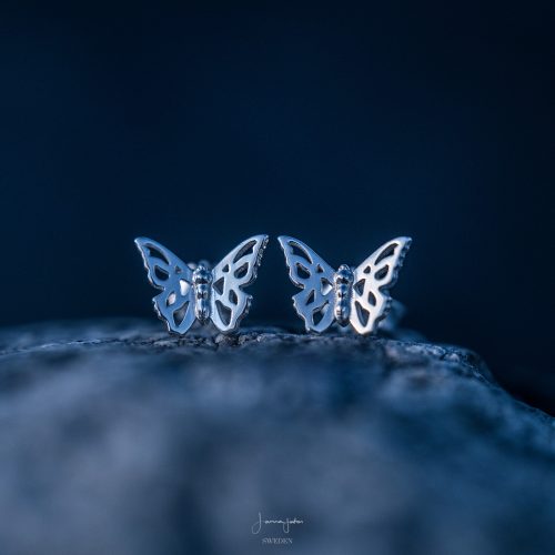 A close up shot of a pair of butterfly studs in Sterling silver against a dark background