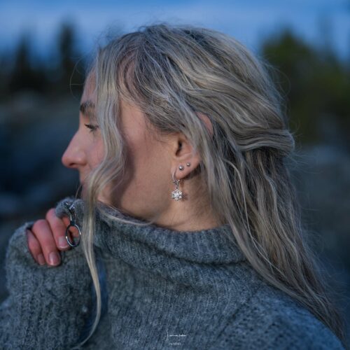 A woman wearing Handcrafted sterling silver snowflake earrings with delicate hoop design.