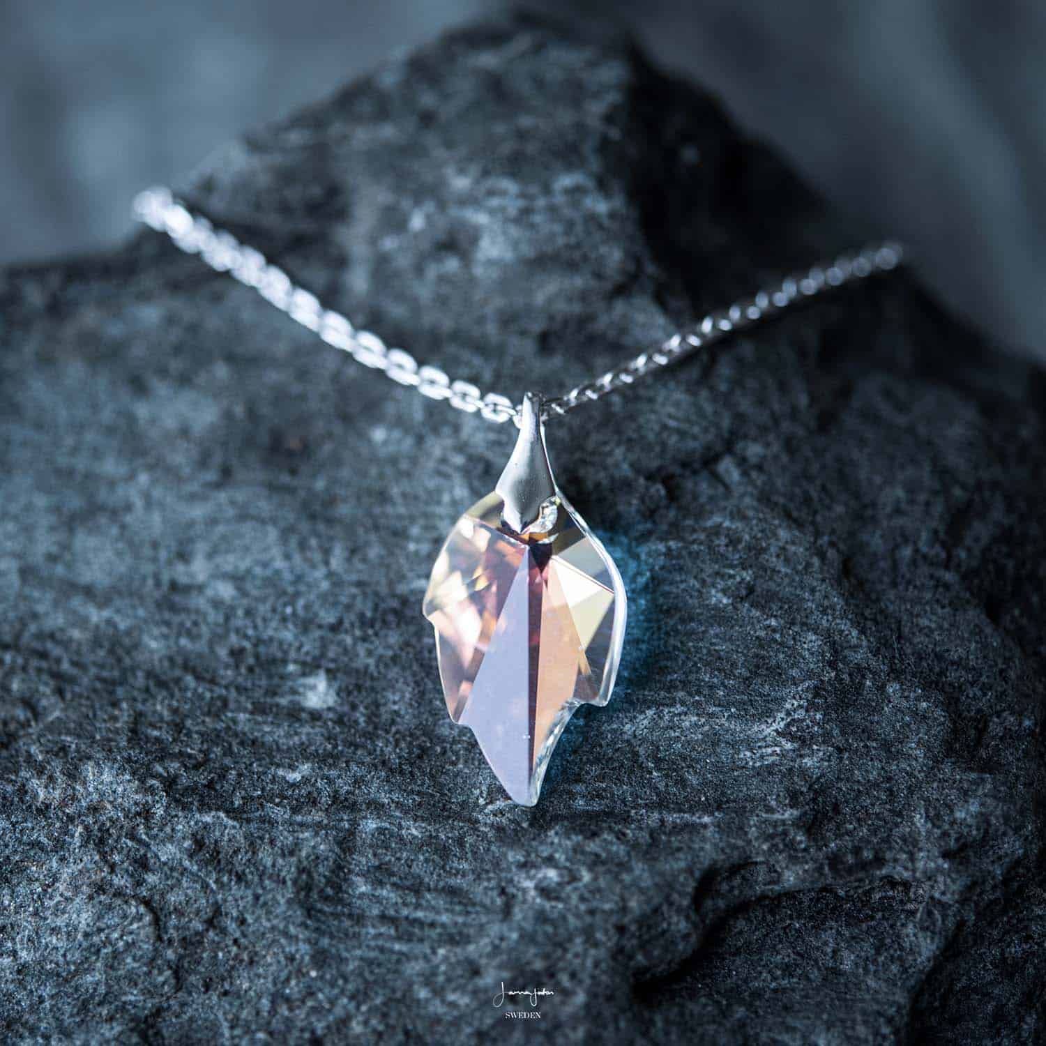 A leaf shaped Swarovski crystal necklace on a silver chain on a dark rock