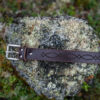 A handcrafted brown leather belt using naturally tanned leather laying on a mossy rock, designed with timeless simplicity, natural beauty, and traditional craftsmanship.