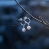 A pair of handcrafted sterling silver pearl earrings with genuine freshwater pearls hanging in a tree