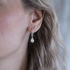 A woman wearing handcrafted sterling silver pearl earrings with genuine freshwater pearls against a dark background