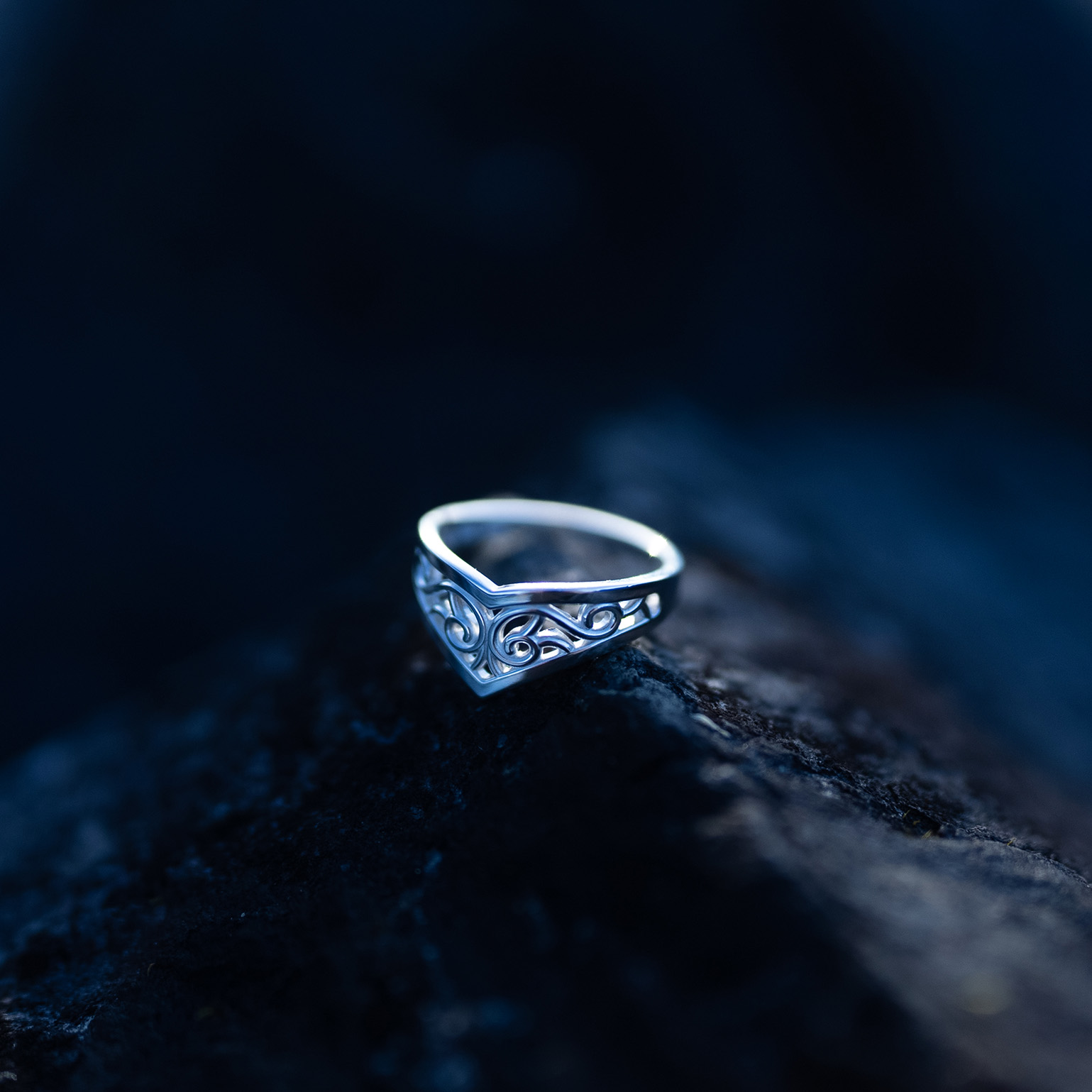 Sterling silver Goddess Ring with an elegant pointed silhouette, intricate engraved details, and a hidden butterfly motif laying on a dark rock