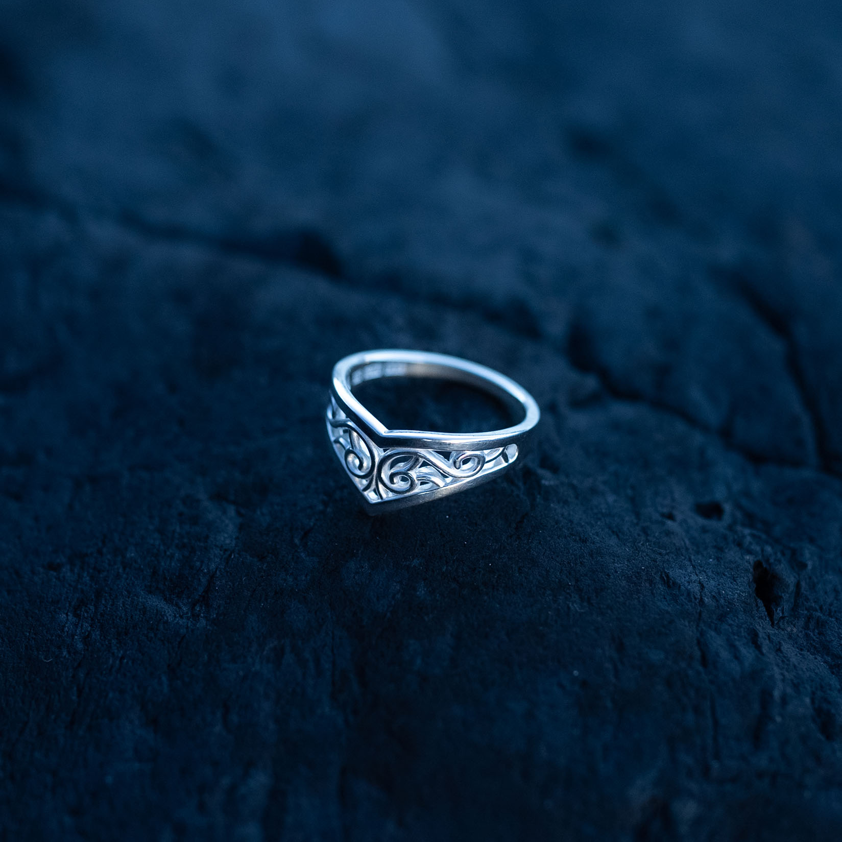Sterling silver Goddess Ring with an elegant pointed silhouette, intricate engraved details, and a hidden butterfly motif laying on a dark rock