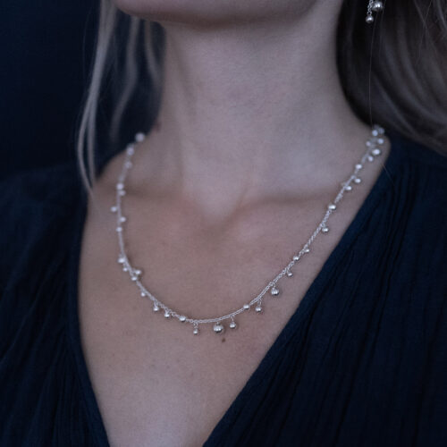 A woman is wearing a sterling silver bead necklace with polished silver beads on a delicate 925 sterling silver chain.
