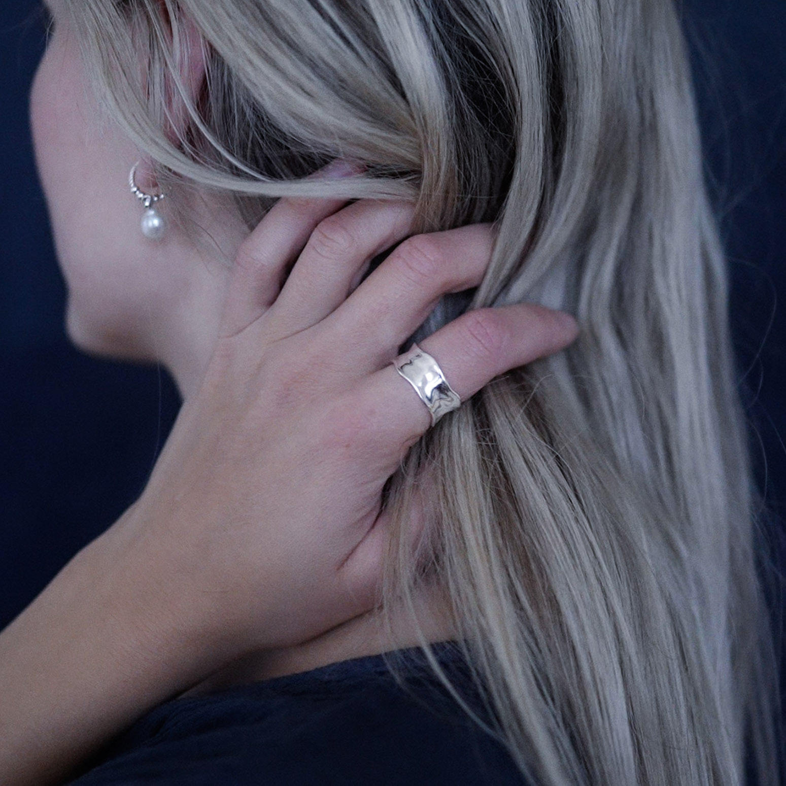 A woman wearing a handcrafted sterling silver water ring with flowing organic curves inspired by waves.
