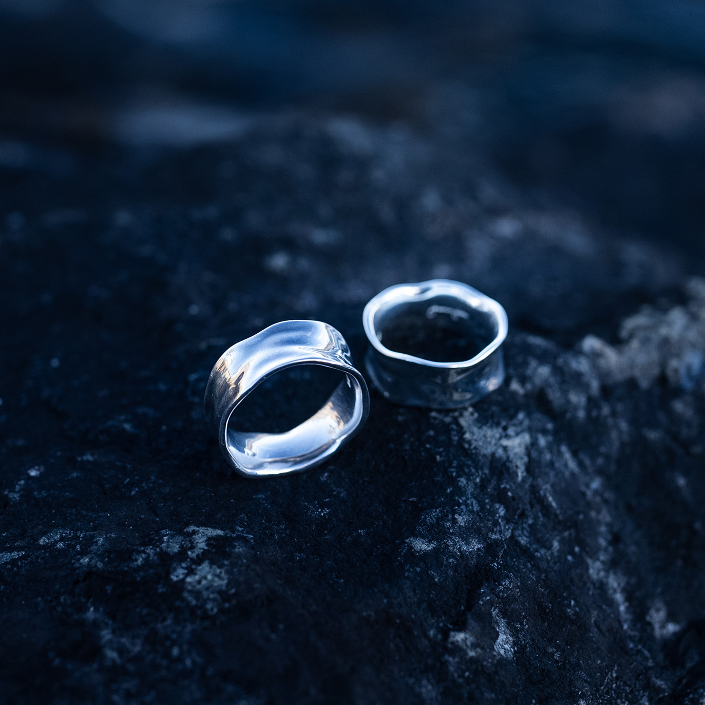 Two handcrafted sterling silver water rings with flowing organic curves inspired by waves laying on a rock