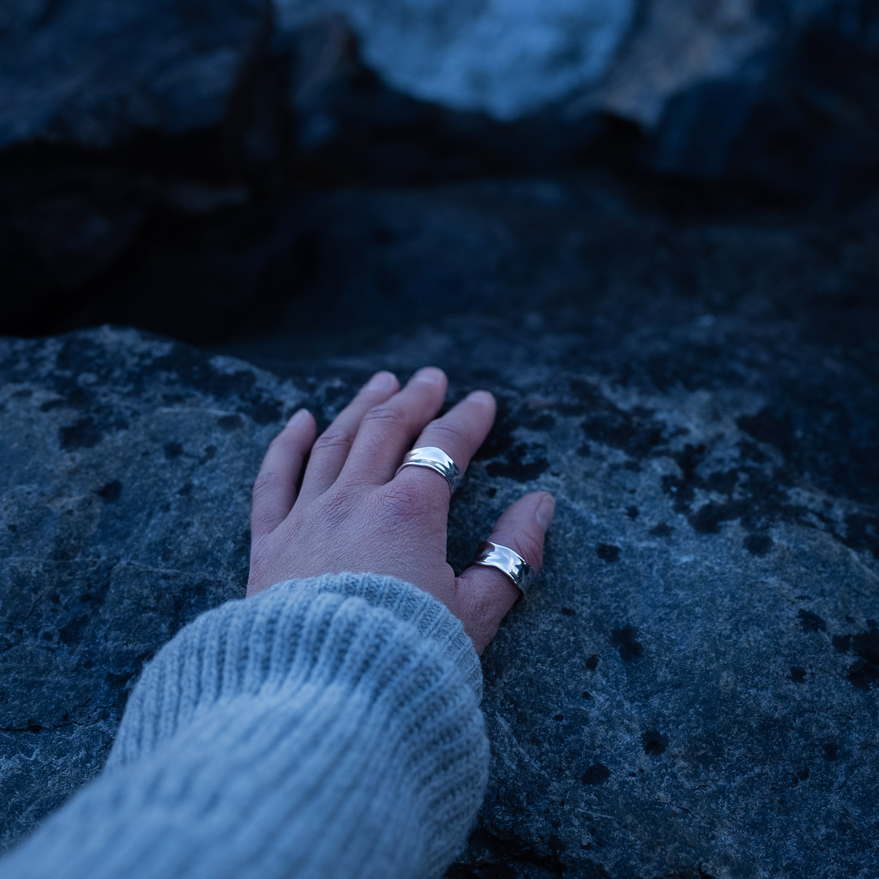 A hand wearing a Handcrafted sterling silver water ring with flowing organic curves inspired by waves.
