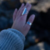 A hand wearing a Handcrafted sterling silver water ring with flowing organic curves inspired by waves.