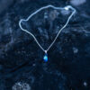 Nebula Necklace with a deep blue Swarovski crystal pendant on a sterling silver chain laying on a rock