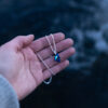 A hand is holding the Nebula Necklace with a deep blue Swarovski crystal pendant on a sterling silver chain,