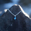 Nebula Necklace with a deep blue Swarovski crystal pendant on a sterling silver chain, is hanging on a stone.