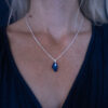 A woman wearing a Nebula Necklace with a deep blue Swarovski crystal pendant on a sterling silver chain,