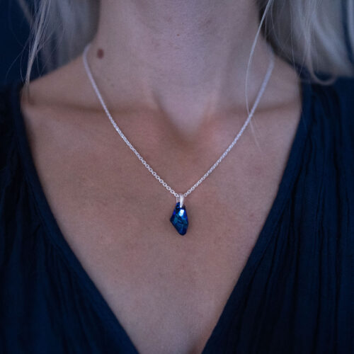 A woman wearing a Nebula Necklace with a deep blue Swarovski crystal pendant on a sterling silver chain,