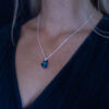 A woman wearing a Nebula Necklace with a deep blue Swarovski crystal pendant on a sterling silver chain,